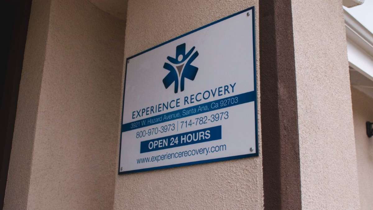 Info sign at the entrance of the Experience Recovery treatment center, with phone numbers, website, address, and opening hours.